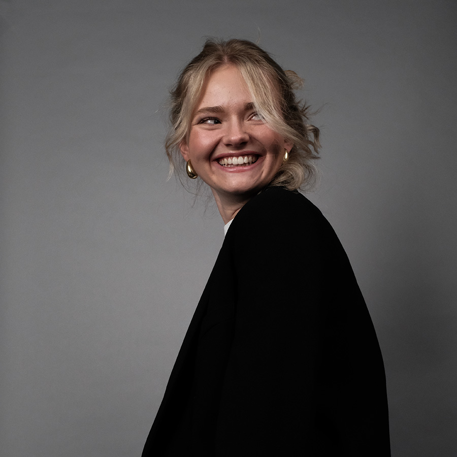 Portrait von Lina, Grafikdesign Studentin, sie trägt ein schwarzes skko, sitzt seitlich und schaut nach rechts während sie breit lacht