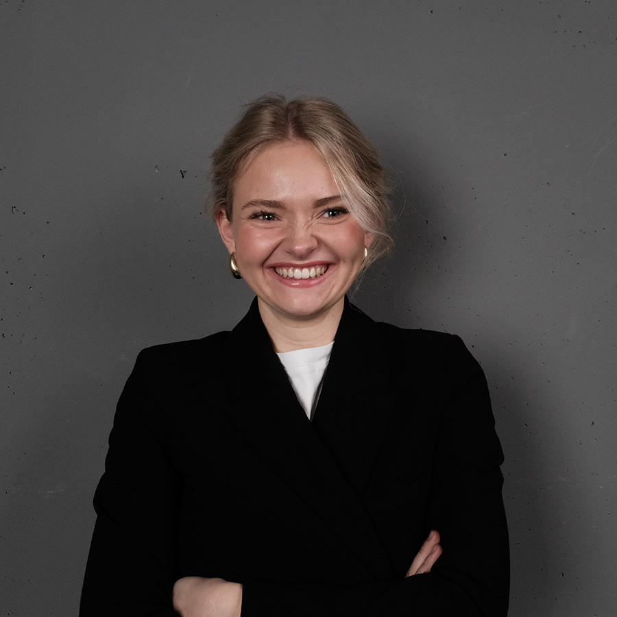 Portrait von Lina, Grafikdesign Studentin, sie trägt eine weißes tshirt und einen schwarzen sakko, siw lacht herzlich und hat verschrenkte arme 