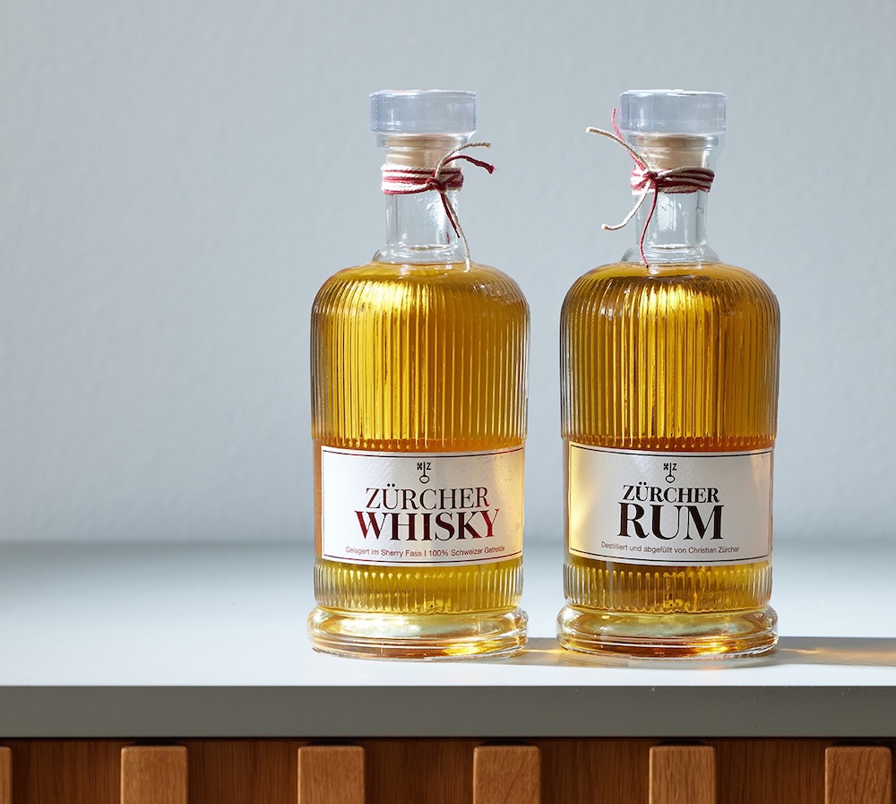 bild eines whisky und rum ettiketts, die flaschen stehen auf einem regal. rechts steht der rum und links der whisky,
                            geschmückt sind die flaschen mit einem rot weißen band, welches an den flaschenhals gebunden ist